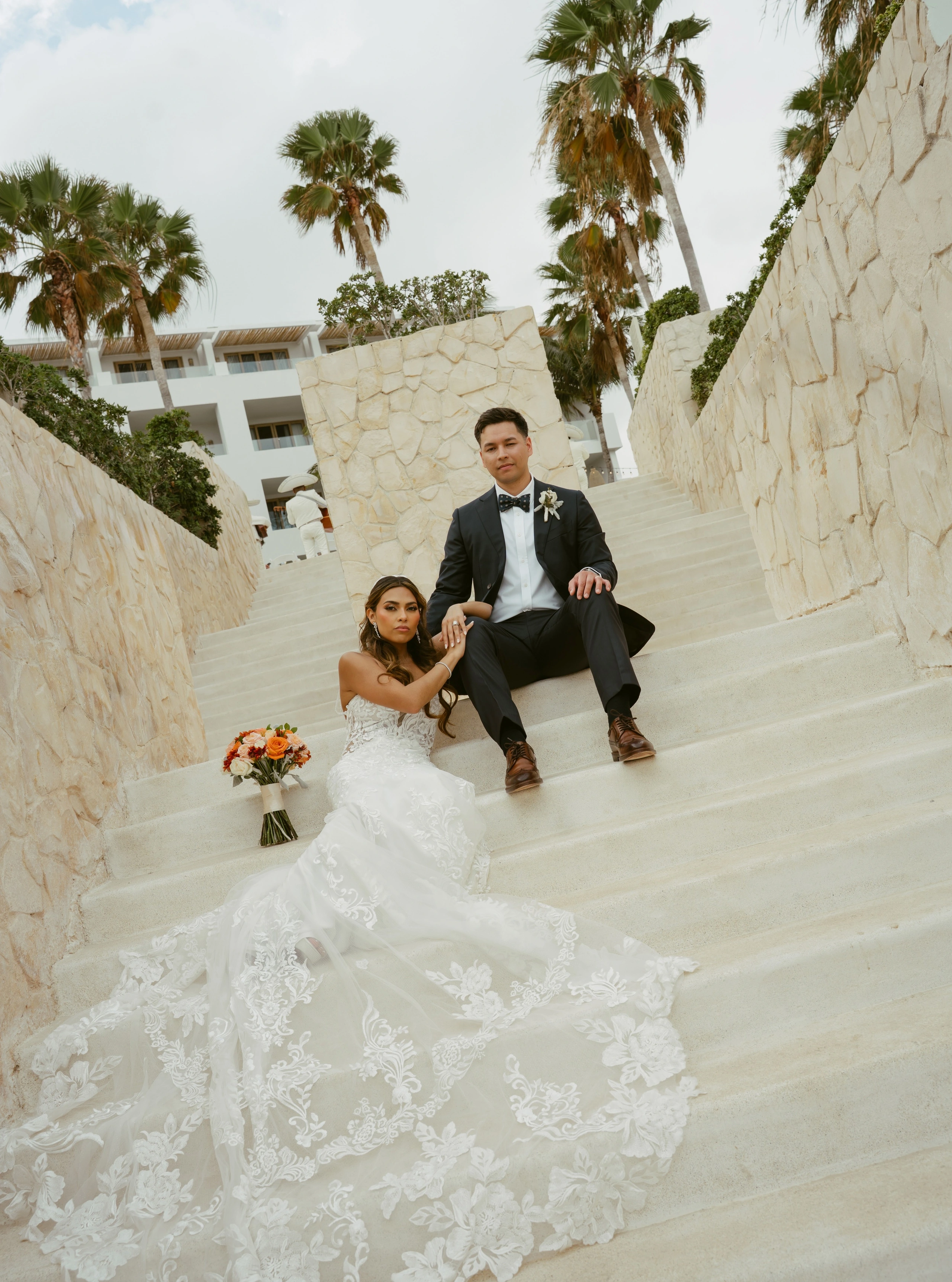 Pareja de recién casados sentada en una escalinata blanca rodeada de vegetación